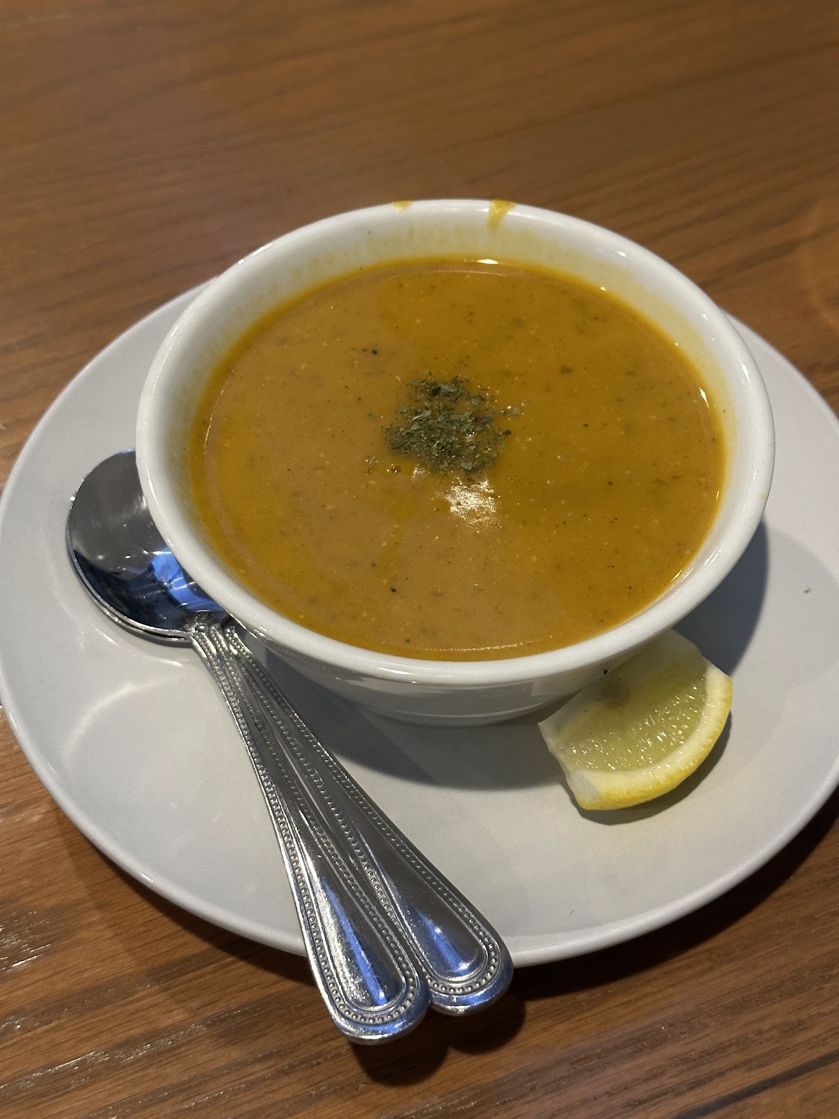 Cup of yellow-orange soup or broth with a lime wedge on a wooden table